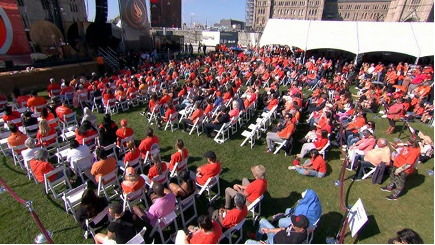 A large outdoor gathering of people seated in front of a stage.