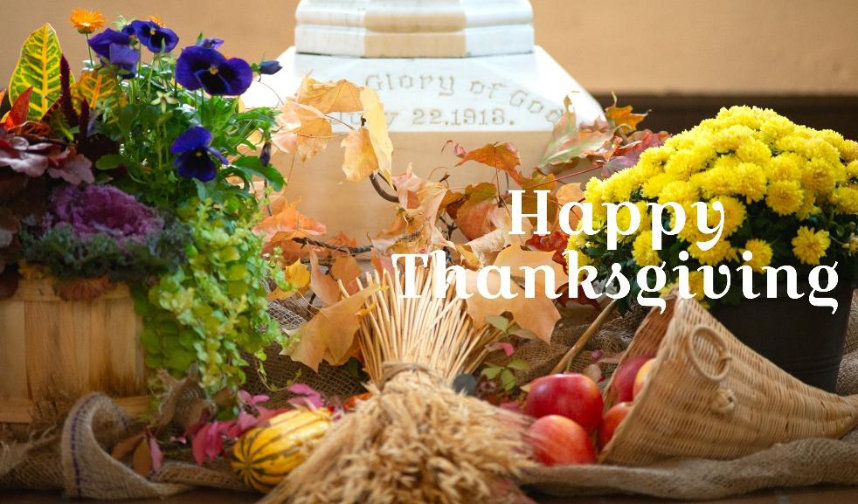 Thanksgiving decorations (fruit, vegetables and a sheaf of wheat) in front of the batismal font with the text Happy Thanksgiving.